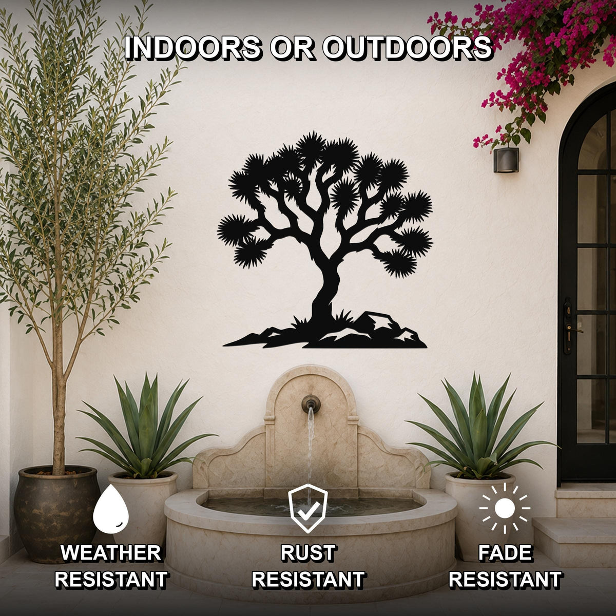 Black metal wall art featuring a Joshua tree silhouette with spiky branches and rocky base, mounted on an outdoor wall above a stone fountain in a patio setting.