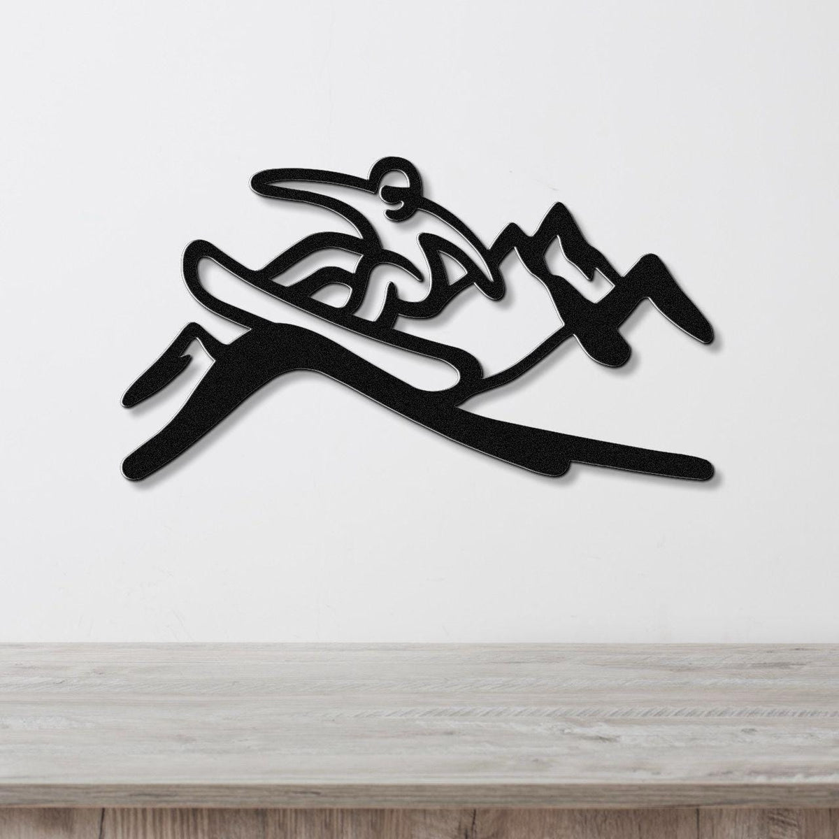 Black metal wall art silhouette of a snowboarder in motion, mounted on a white wall above a light wood surface.