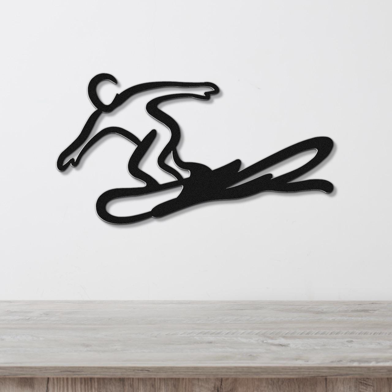 Black metal wall art silhouette of a snowboarder in motion, mounted on a white wall above a light wood counter.