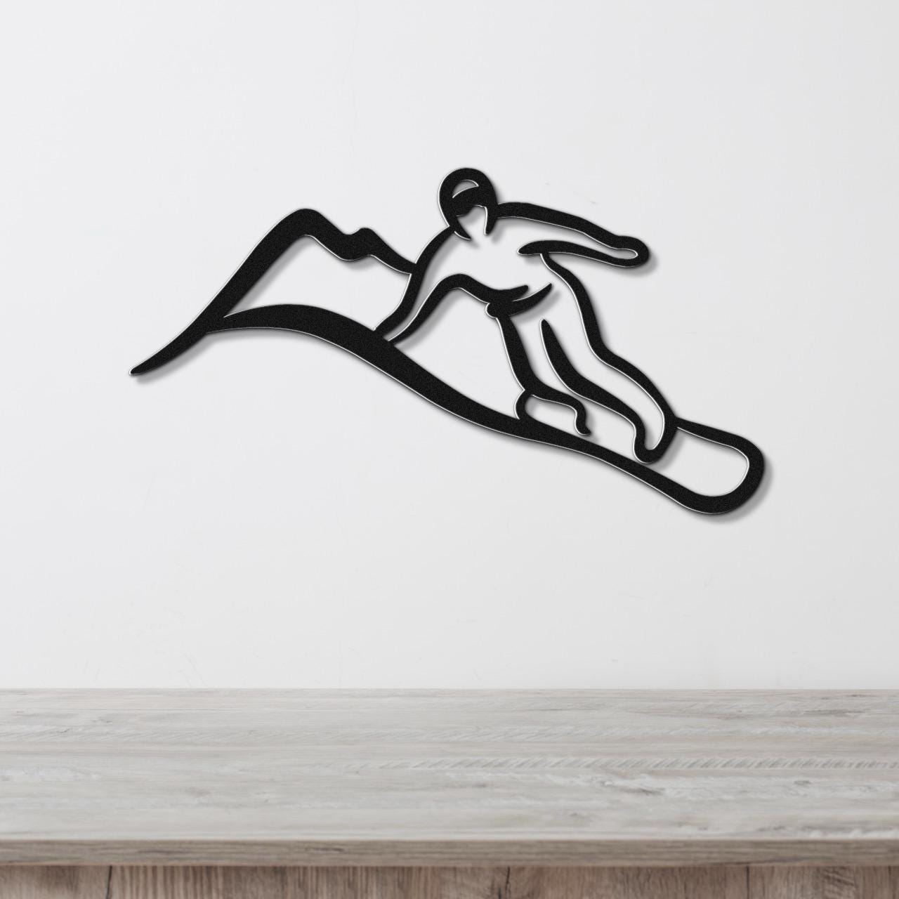 Black metal wall art silhouette of a snowboarder in motion, mounted on a white wall above a light wood surface.