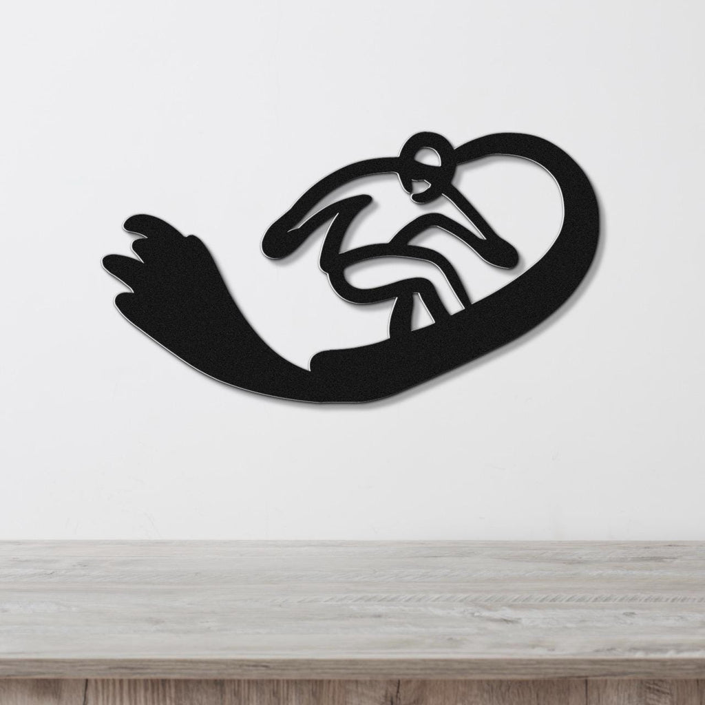 Black metal wall art silhouette of a snowboarder in motion, mounted on a white wall above a light wood surface.