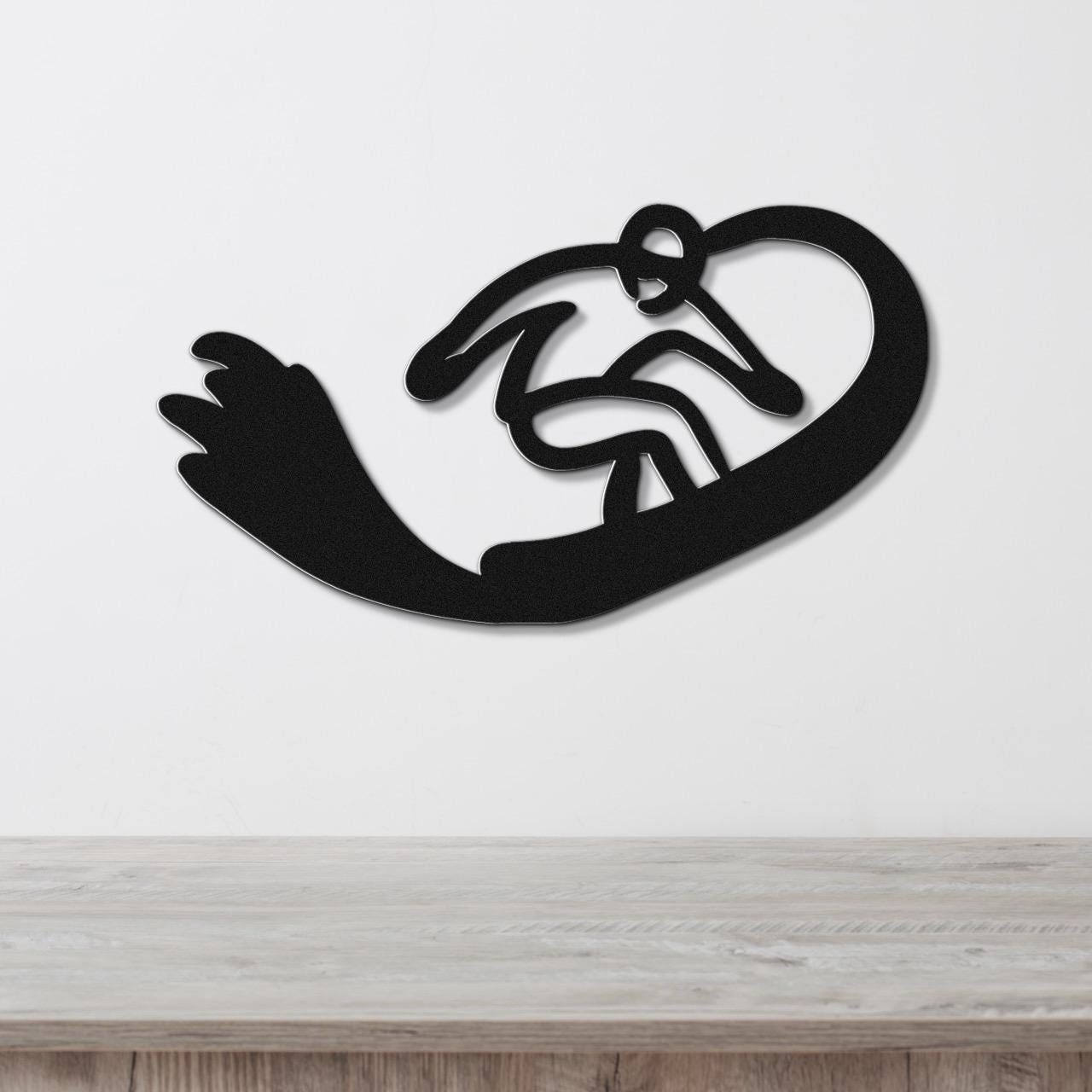 Black metal wall art silhouette of a snowboarder in motion, mounted on a white wall above a light wood surface.