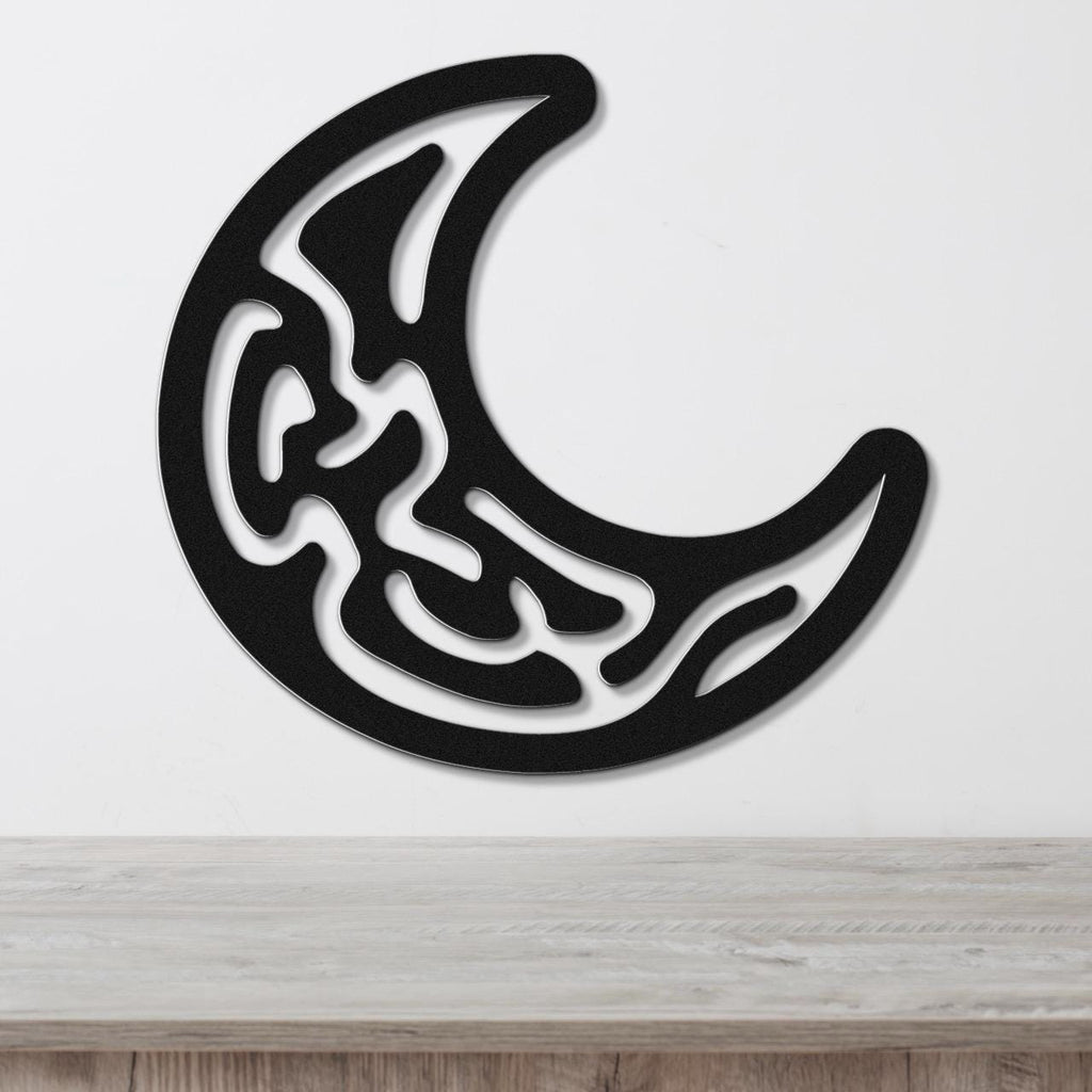 Black metal crescent moon wall art with intricate internal cutout patterns, mounted on a white wall above a light wood surface.