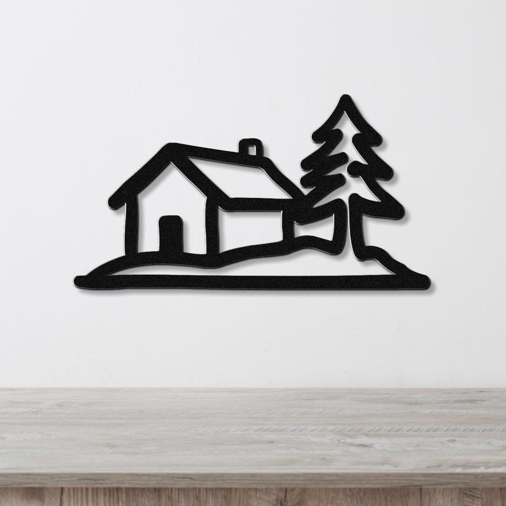 Black metal wall art cutout of a cabin and pine tree silhouette, mounted on a white wall above a light wood counter.