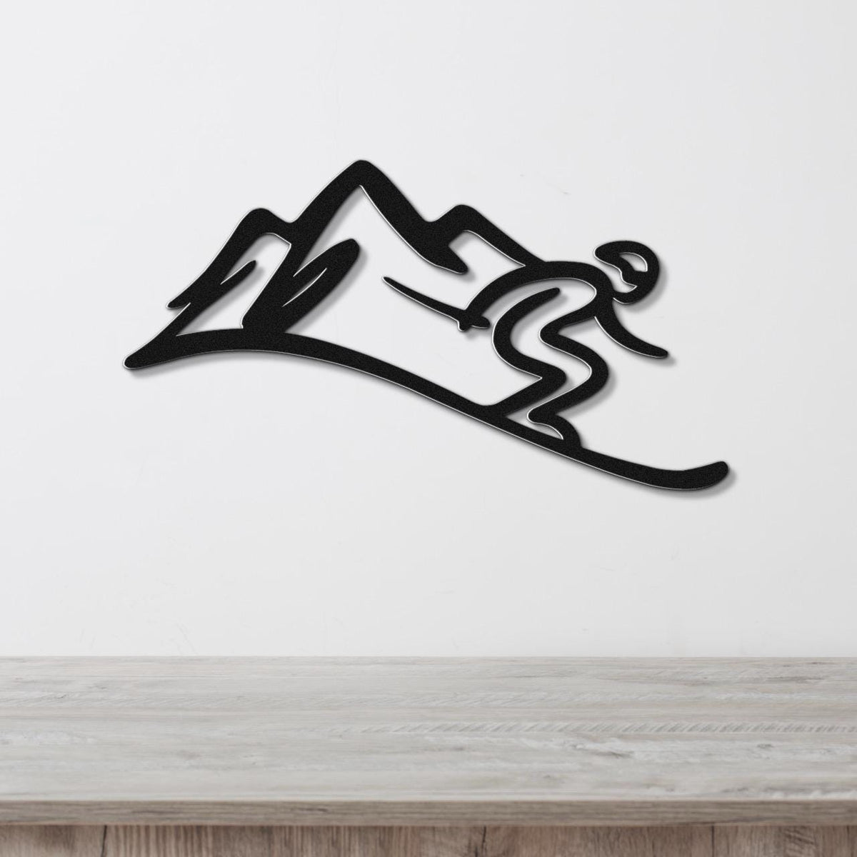 Black metal wall art featuring a skier silhouette in motion against mountain peaks, mounted on a white wall above a light wood surface.