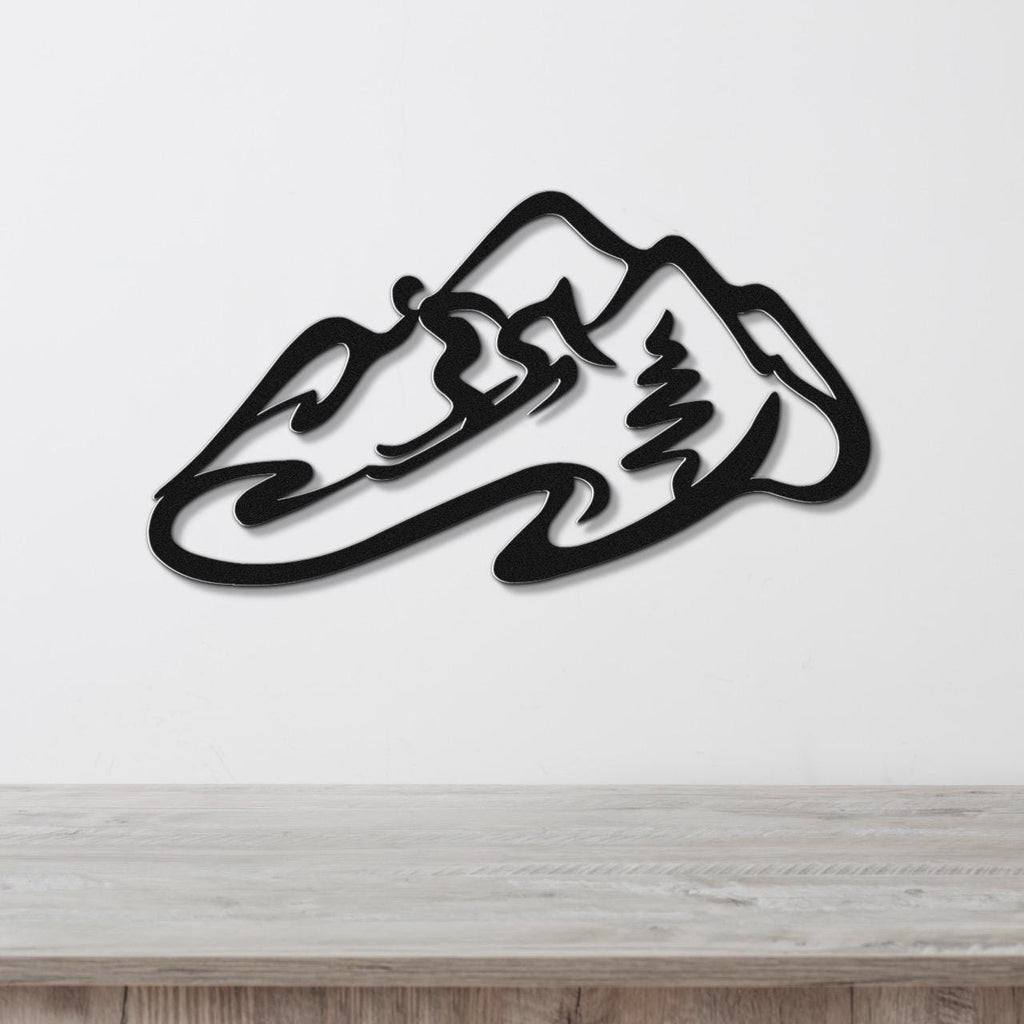 Black metal wall art featuring a minimalist skier silhouette and mountain range cutout, mounted on a white wall above a wooden surface.