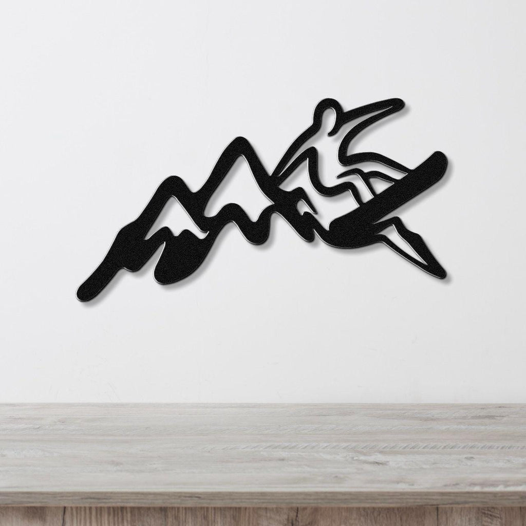 Black metal wall art featuring a snowboarder silhouette cutting through mountain peaks, mounted on a white wall above a wooden counter.