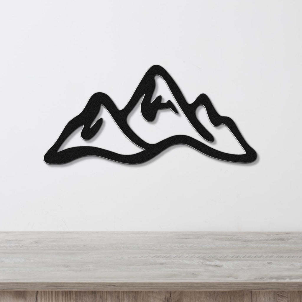 Black metal wall art in a mountain range silhouette design, mounted on a white wall above a light wood surface.