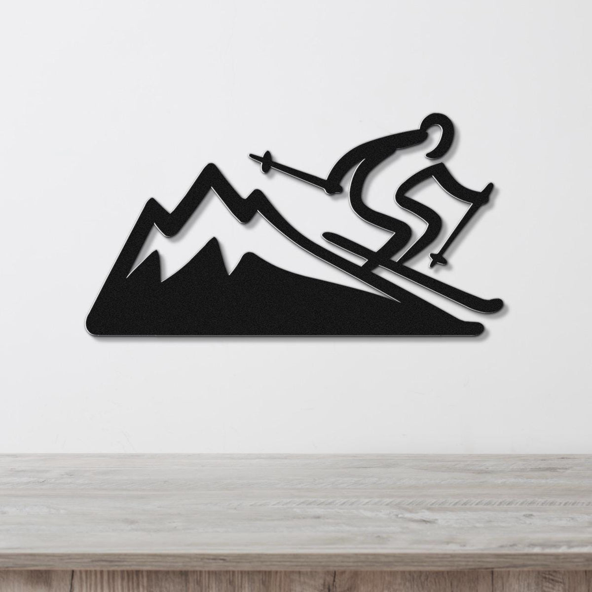 Black metal wall sculpture of a skier descending a mountain, mounted on a white wall above a wooden surface.
