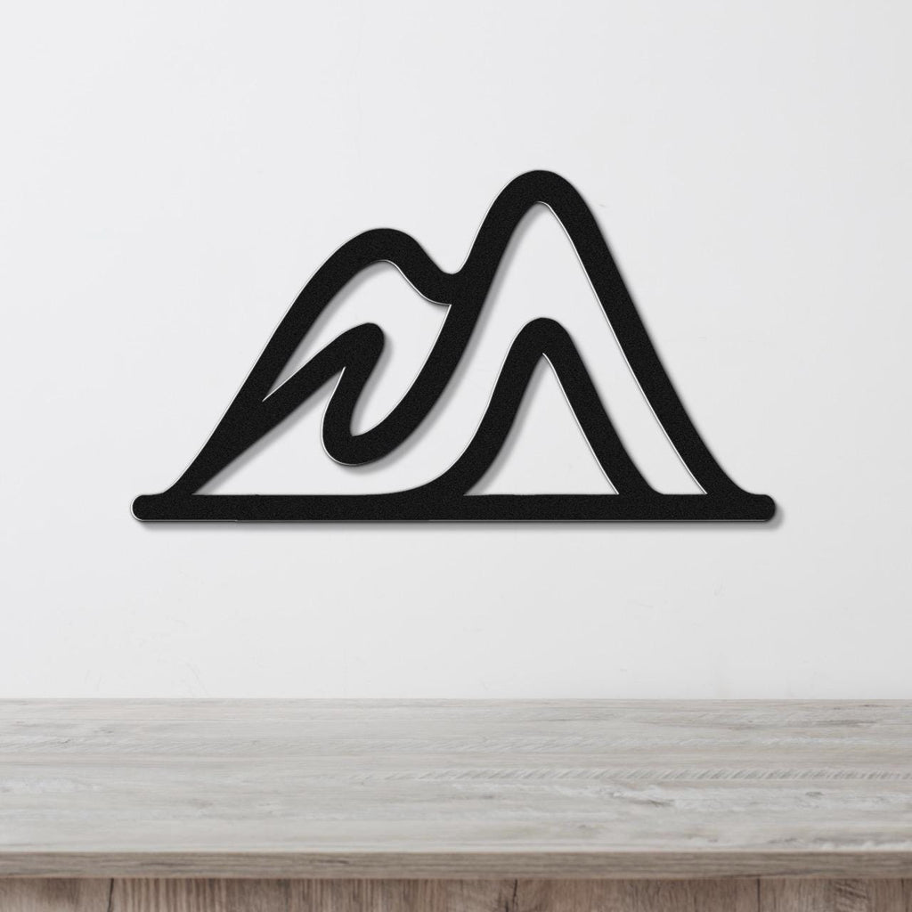 Black metal wall art with a mountain silhouette design, featuring layered peaks and internal cutouts, mounted on a white wall above a wooden surface.