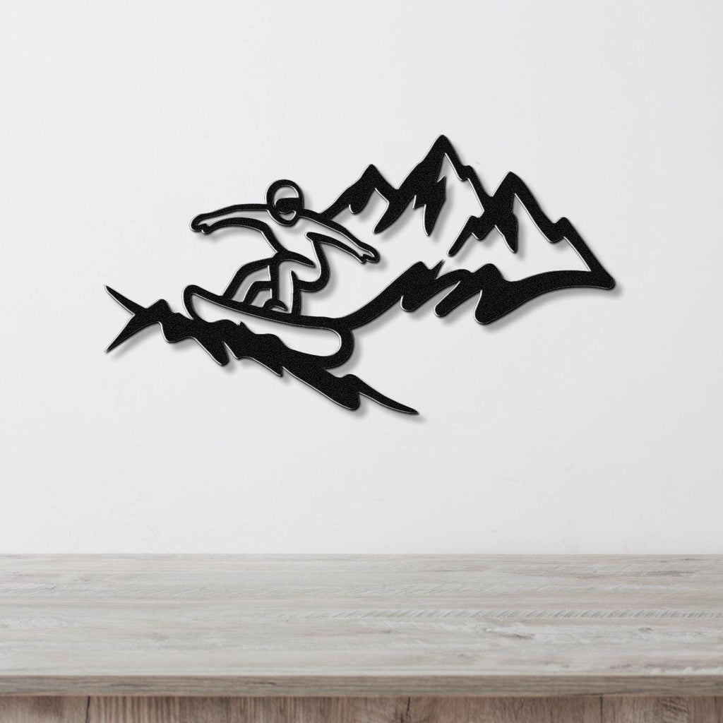 Black metal wall art featuring a snowboarder silhouette in motion against mountain peaks, mounted on a white wall above a wooden surface.