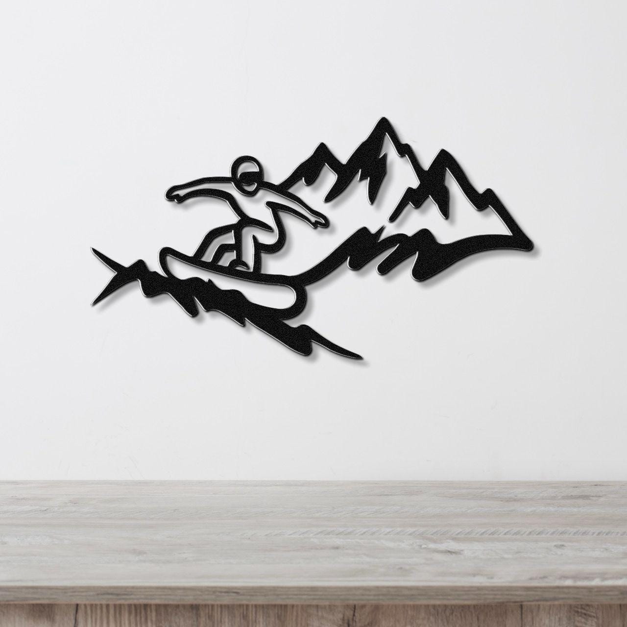 Black metal wall art featuring a snowboarder silhouette in motion against mountain peaks, mounted on a white wall above a wooden surface.