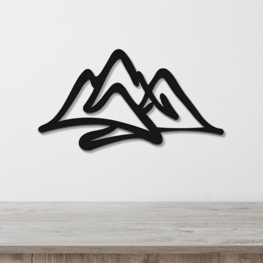Black metal wall art with a layered mountain silhouette design, mounted on a white wall above a light wood surface.