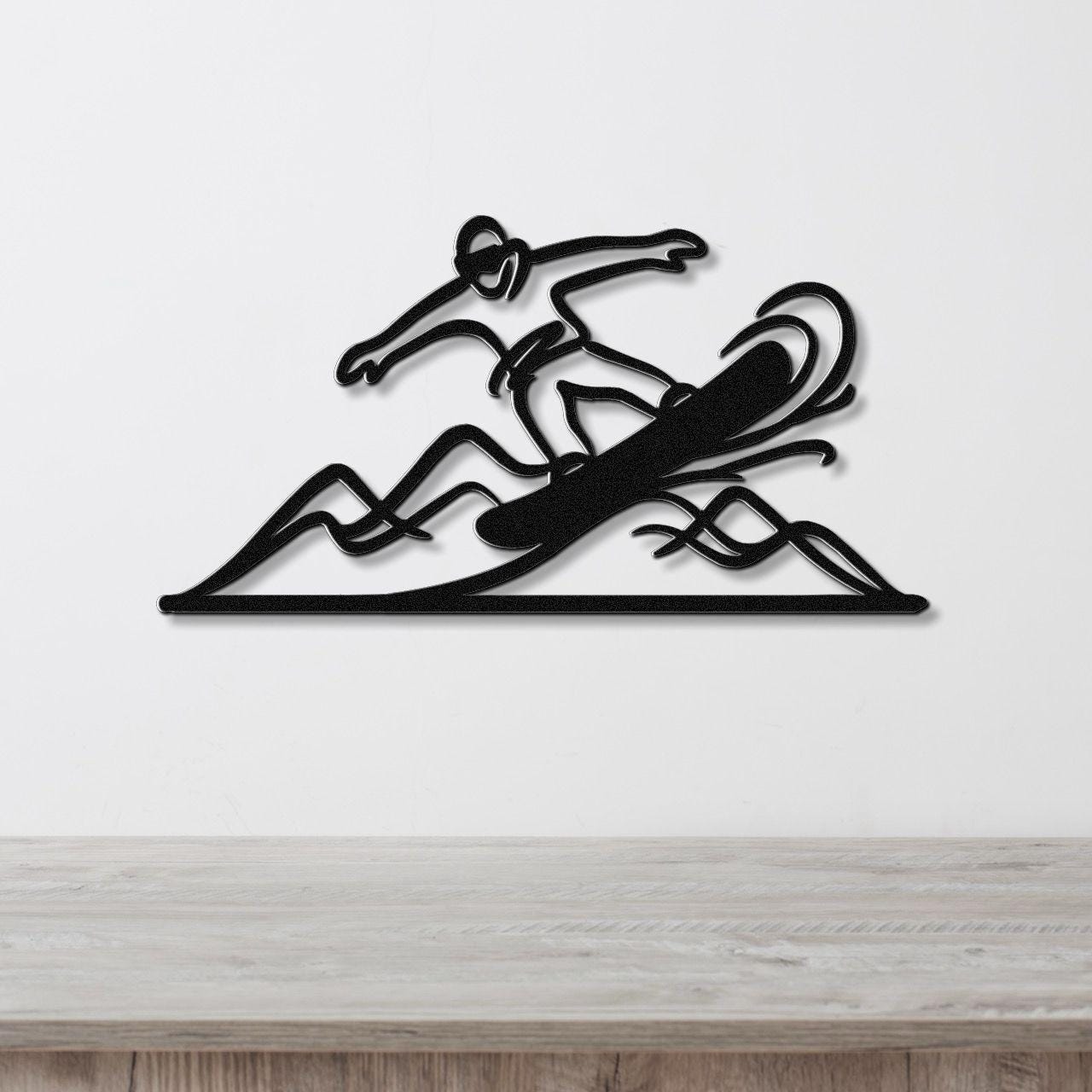 Black metal wall art featuring a snowboarder in motion over mountain shapes, mounted on a white wall above a wooden surface.