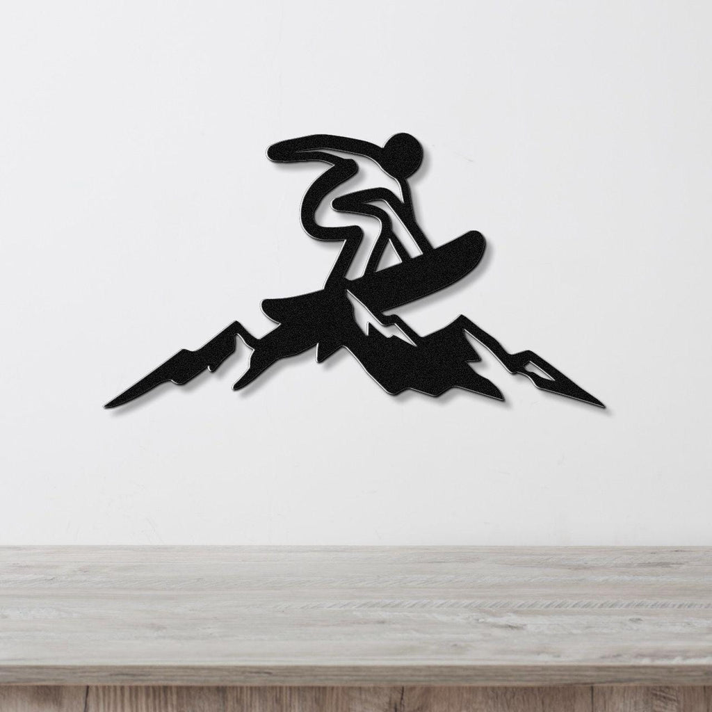 Black metal wall art featuring a snowboarder silhouette in motion above mountain peaks, mounted on a white wall above a wooden counter.
