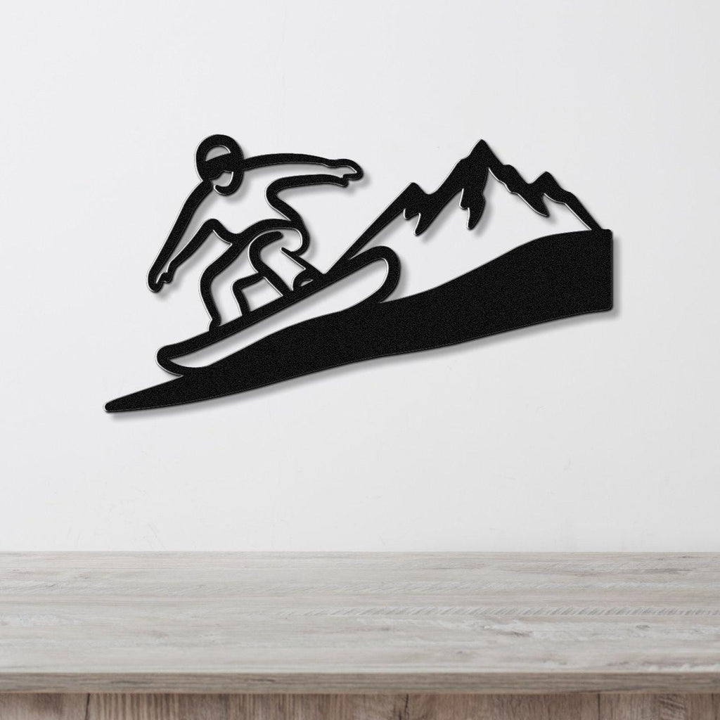 Black metal wall art featuring a snowboarder silhouette in motion above a mountain range, mounted on a white wall above a wooden counter.