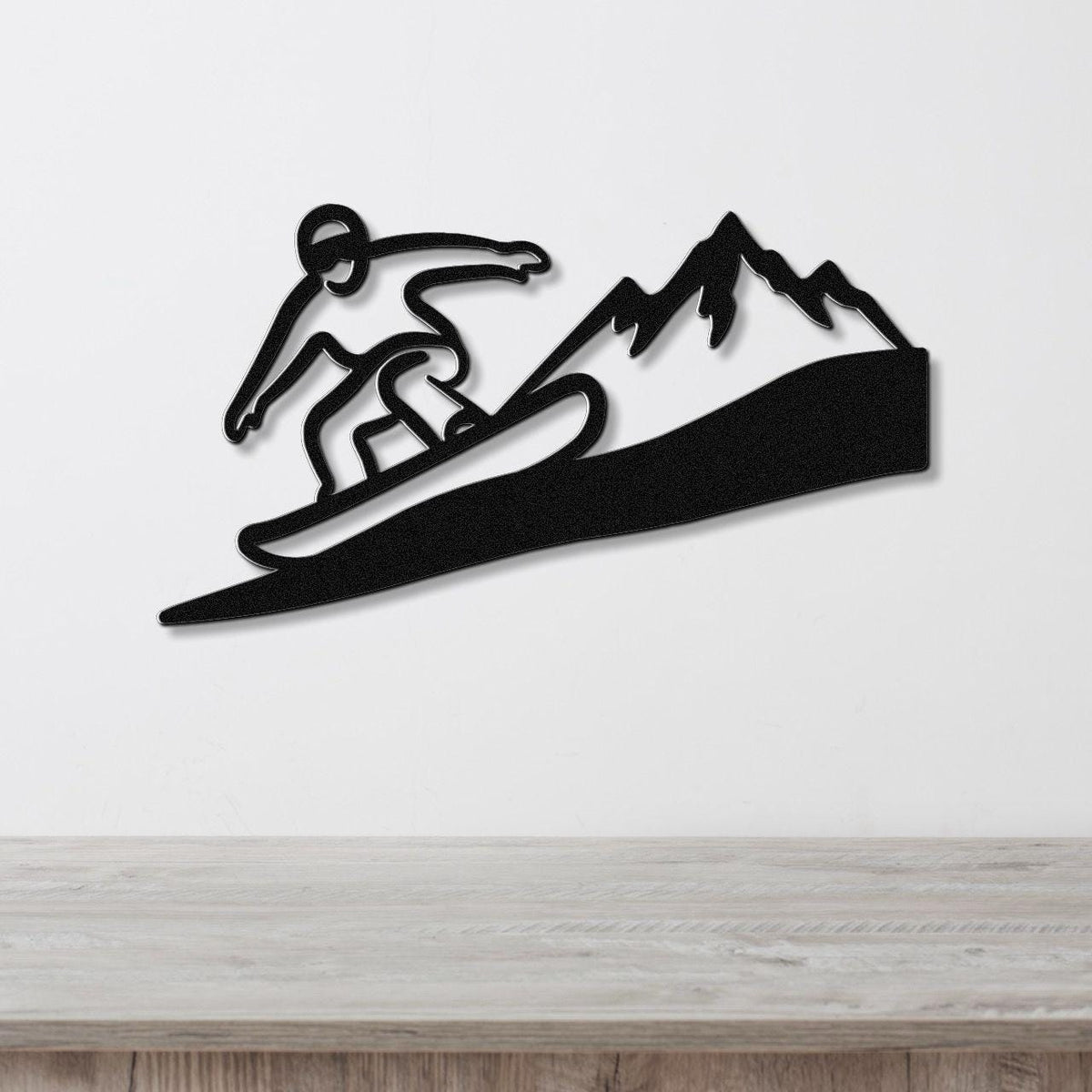 Black metal wall art featuring a snowboarder silhouette in motion above a mountain range, mounted on a white wall above a wooden counter.