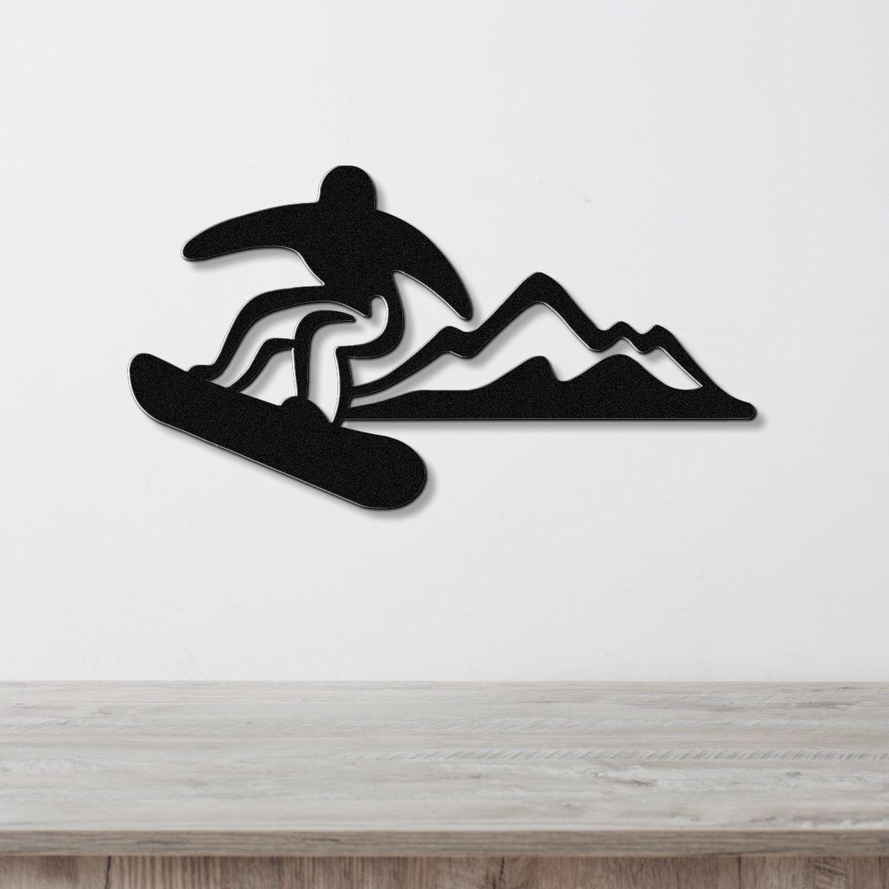 Black metal wall art featuring a snowboarder silhouette in dynamic motion above a mountain range, mounted on a white wall above a wooden counter.