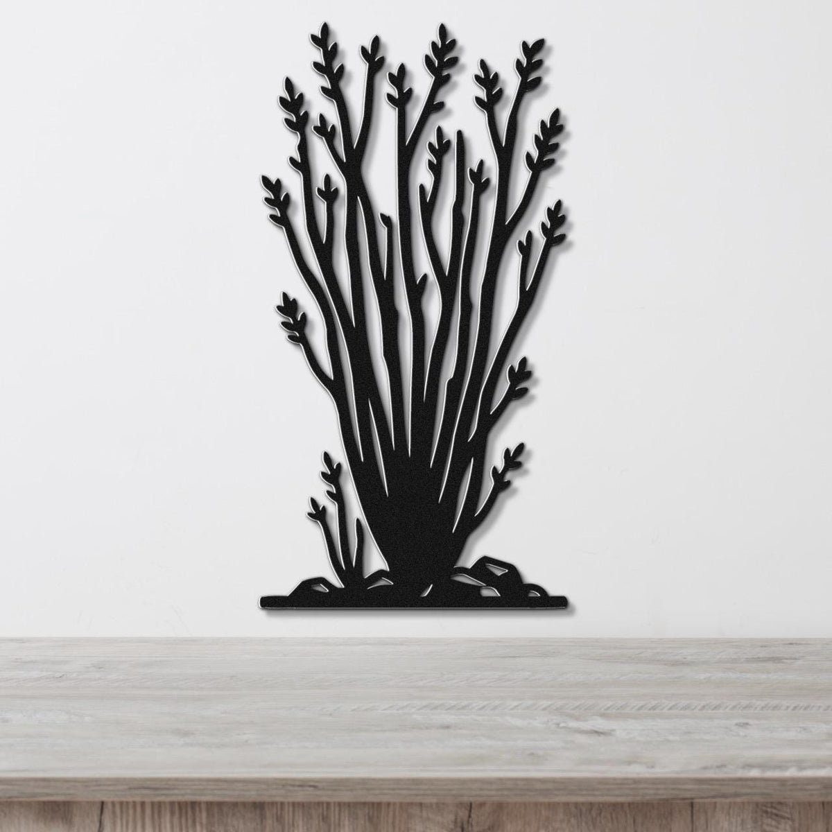 Black metal wall art cutout of an ocotillo plant with branching stems and leaf clusters, mounted on a white wall above a light wood surface.