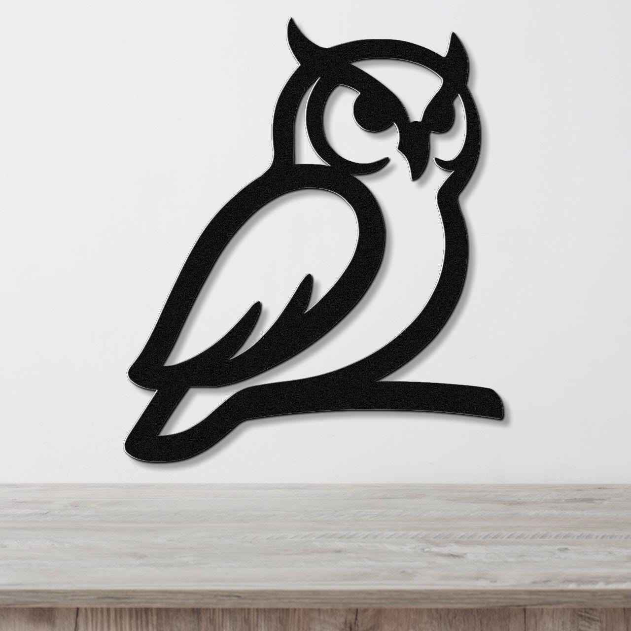 Black metal owl wall art with a cutout design, mounted on a white wall above a wooden surface.