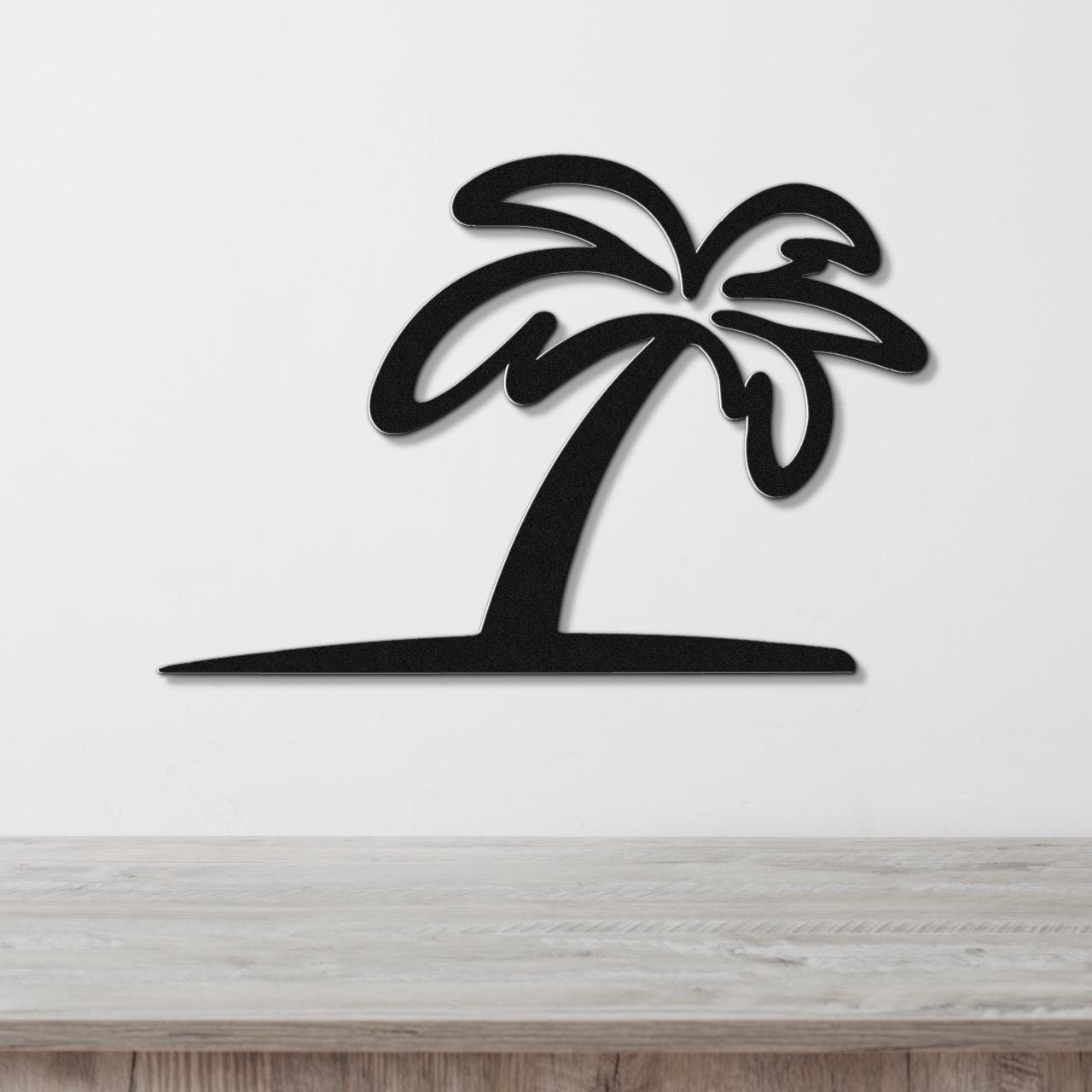 Black metal palm tree wall art with a silhouette cutout design, mounted on a white wall above a light wood surface.