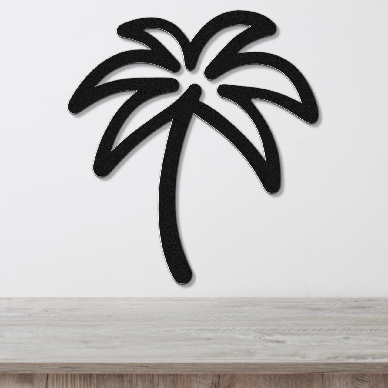 Black metal palm tree wall art with a cutout silhouette design, mounted on a white wall above a light wood surface.