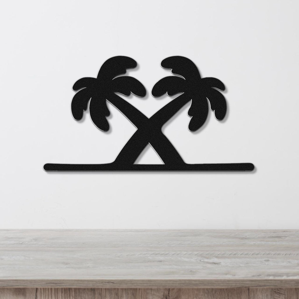 Black metal wall art featuring a silhouette of two crossed palm trees with leafy fronds, mounted on a white wall above a light wood surface.