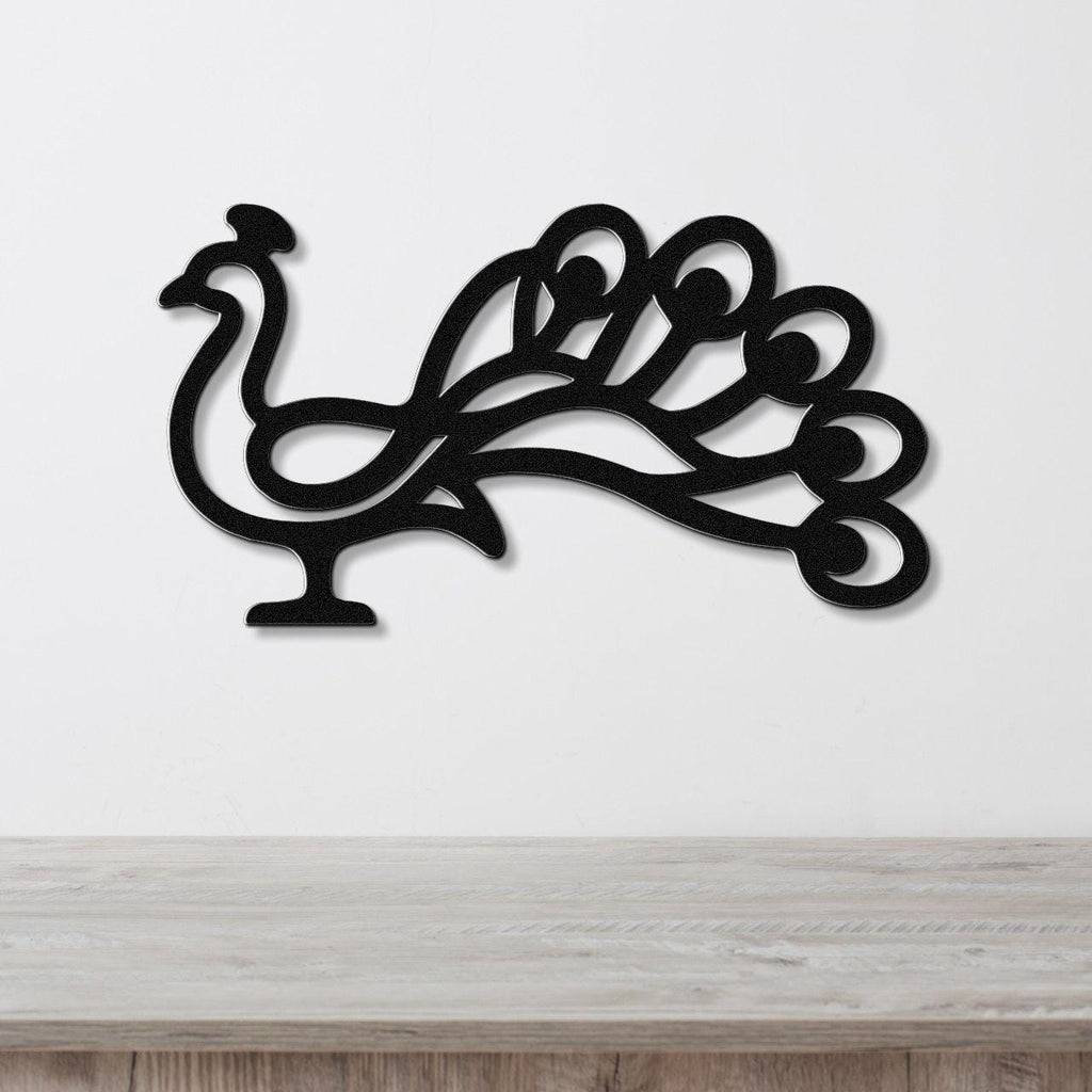Black metal peacock wall art with a cutout silhouette of a bird and fanned tail, mounted on a white wall above a light wood surface.