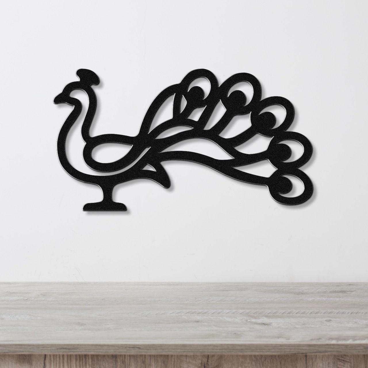 Black metal peacock wall art with a cutout silhouette of a bird and fanned tail, mounted on a white wall above a light wood surface.
