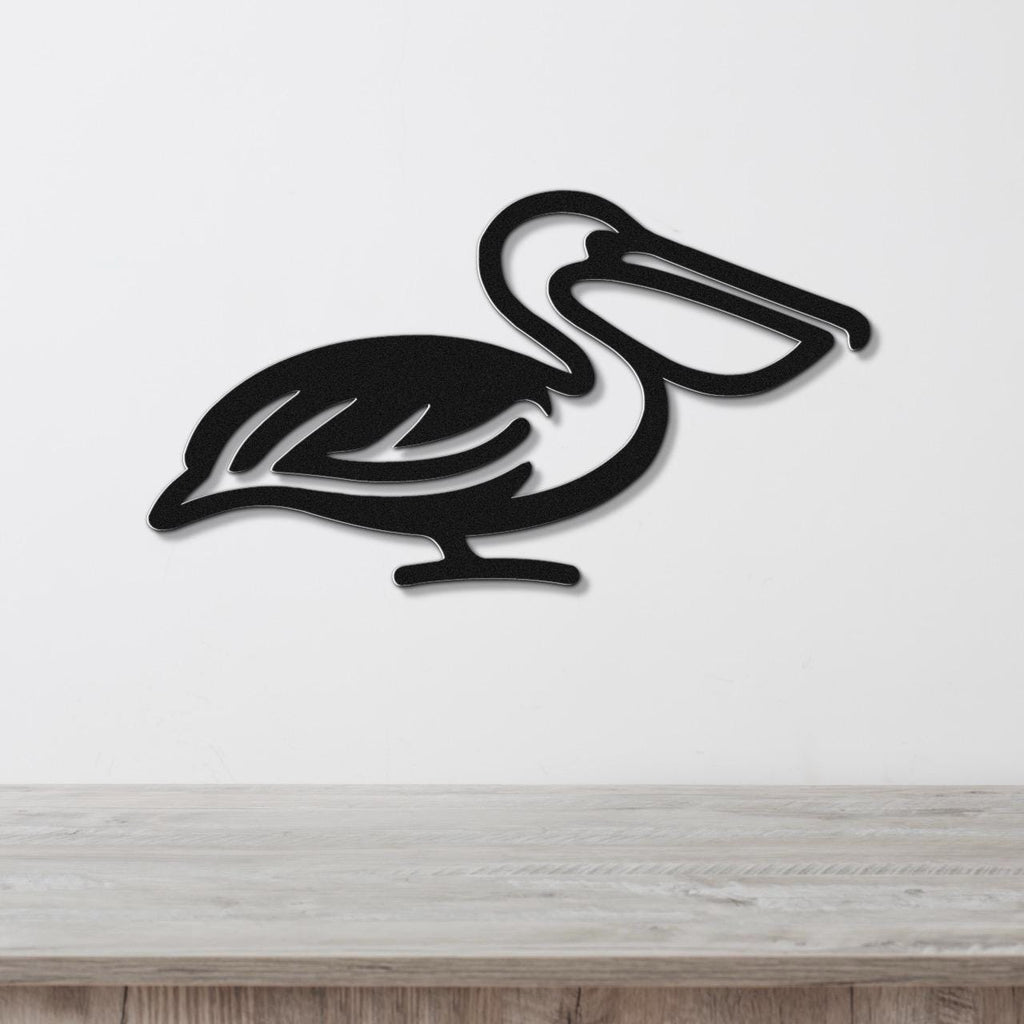 Black metal pelican wall art with a cutout silhouette design, mounted on a white wall above a light wood surface.