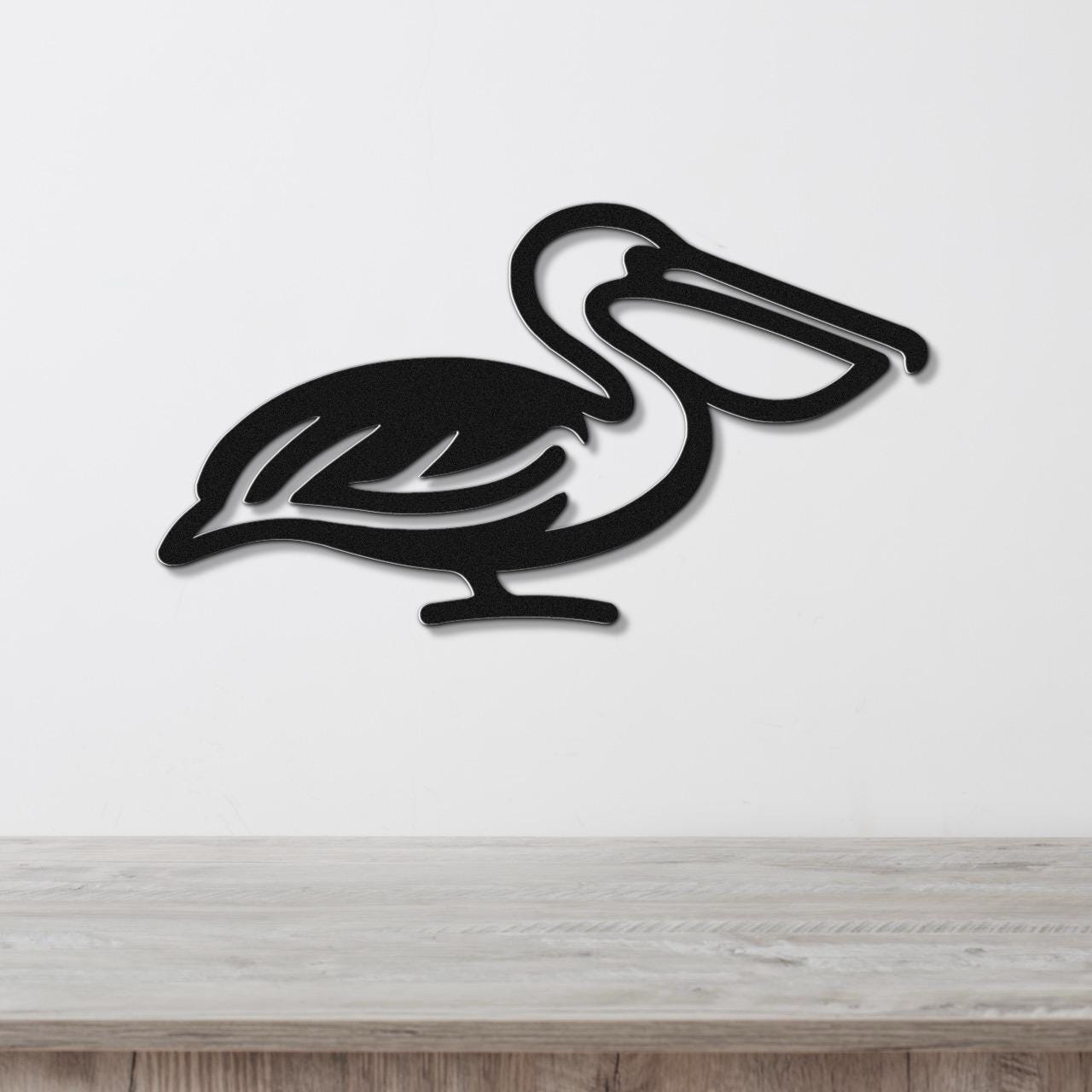 Black metal pelican wall art with a cutout silhouette design, mounted on a white wall above a light wood surface.
