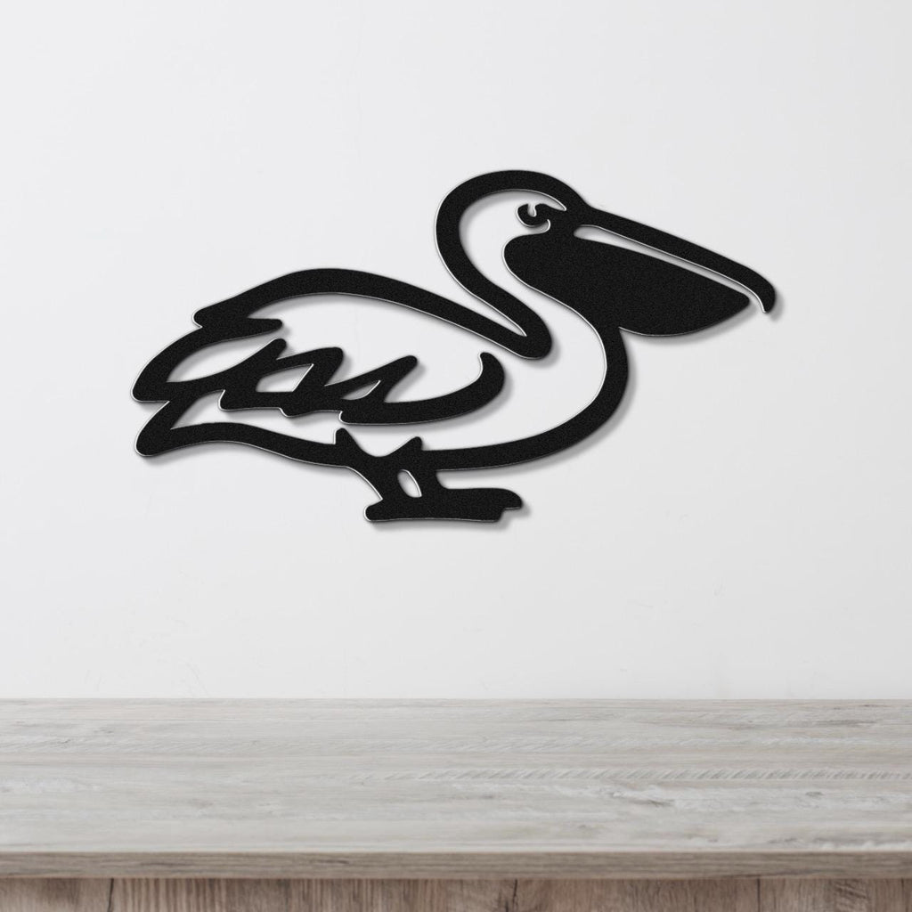 Black metal pelican wall art with a cutout silhouette design, mounted on a white wall above a light wood surface.