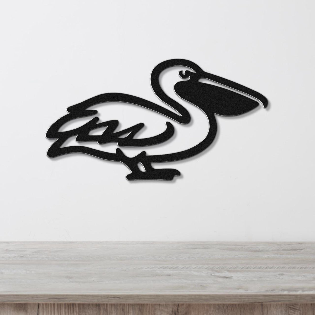 Black metal pelican wall art with a cutout silhouette design, mounted on a white wall above a light wood surface.