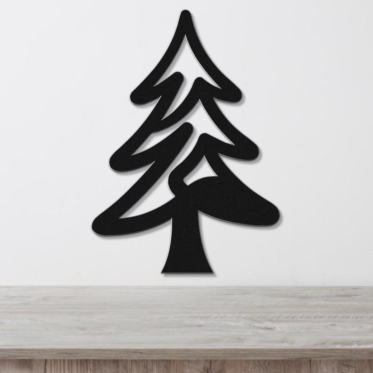 Black metal pine tree wall art with layered branch cutouts, mounted on a white wall above a light wood counter.