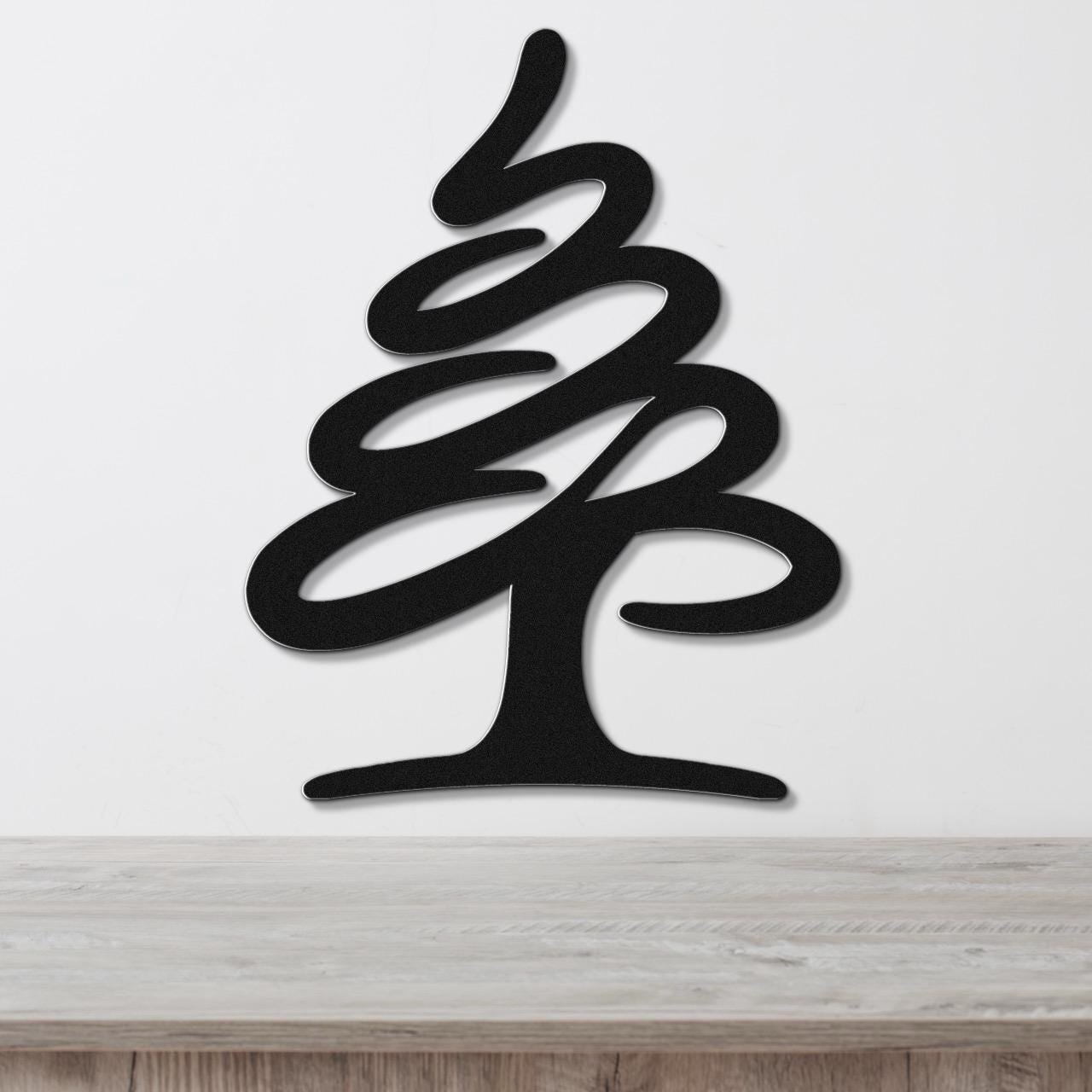 Black metal wall art in a stylized pine tree silhouette with layered curves, mounted on a white wall above a light wood surface.