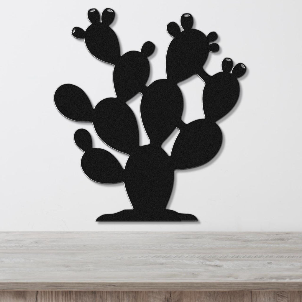 Black metal cactus wall art with multiple paddle-shaped segments and internal cutouts, mounted on a white wall above a light wood surface.