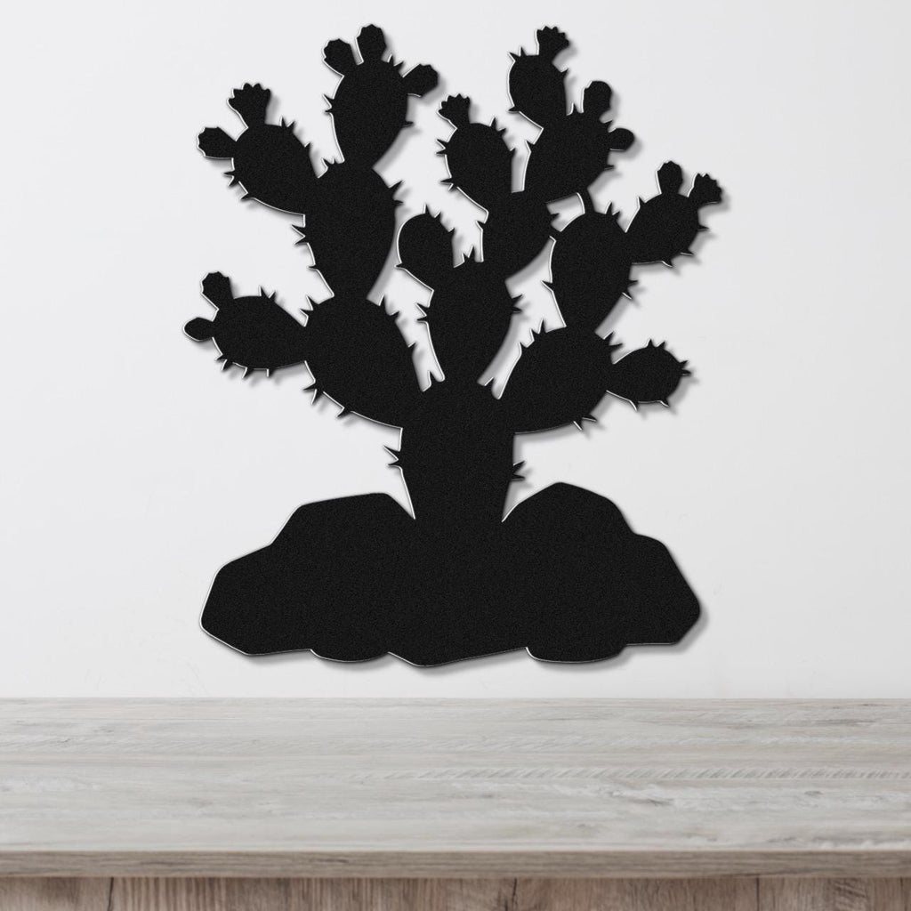 Black metal wall art cutout of a prickly pear cactus with multiple pads and spines, mounted on a white wall above a light wood surface.