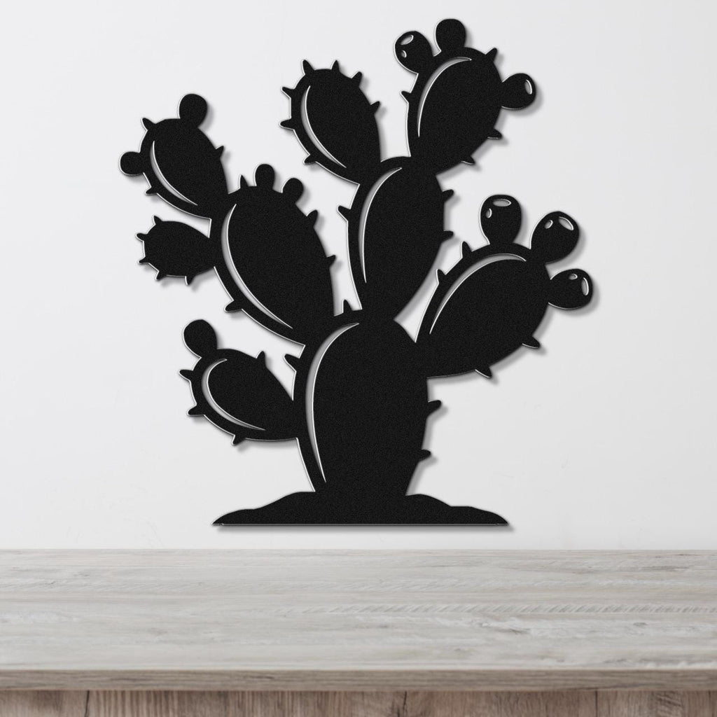 Black metal cactus wall art with multiple paddle-shaped segments and spines, mounted on a white wall above a light wood surface.