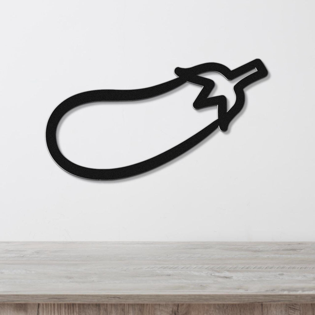 Black metal eggplant wall art with a bold silhouette and stem cutout, mounted on a white wall above a light wood countertop.