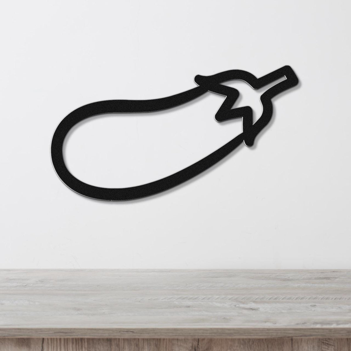 Black metal eggplant wall art with a bold silhouette and stem cutout, mounted on a white wall above a light wood countertop.