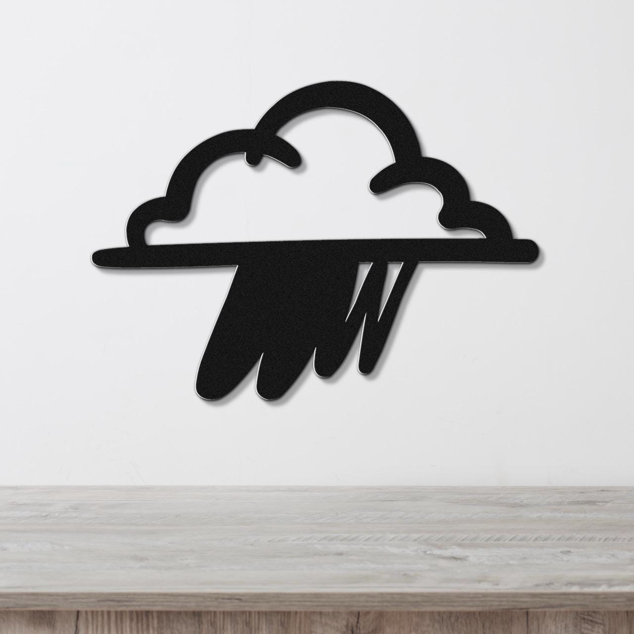 Black metal wall art in the shape of a rain cloud with raindrop cutouts, mounted on a white wall above a wooden surface.