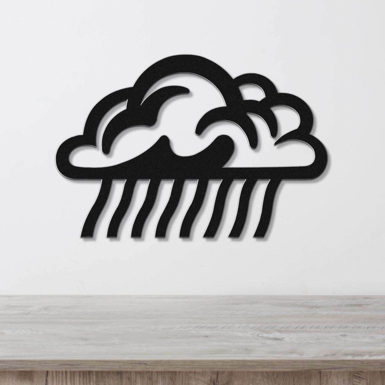 Black metal wall art cutout of a rain cloud with raindrop lines, mounted on a white wall above a wooden surface.