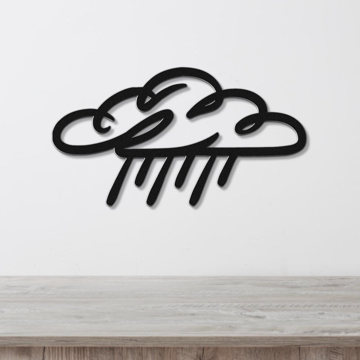 Black metal wall art in a cloud and raindrop silhouette design, mounted on a white wall above a light wood surface.