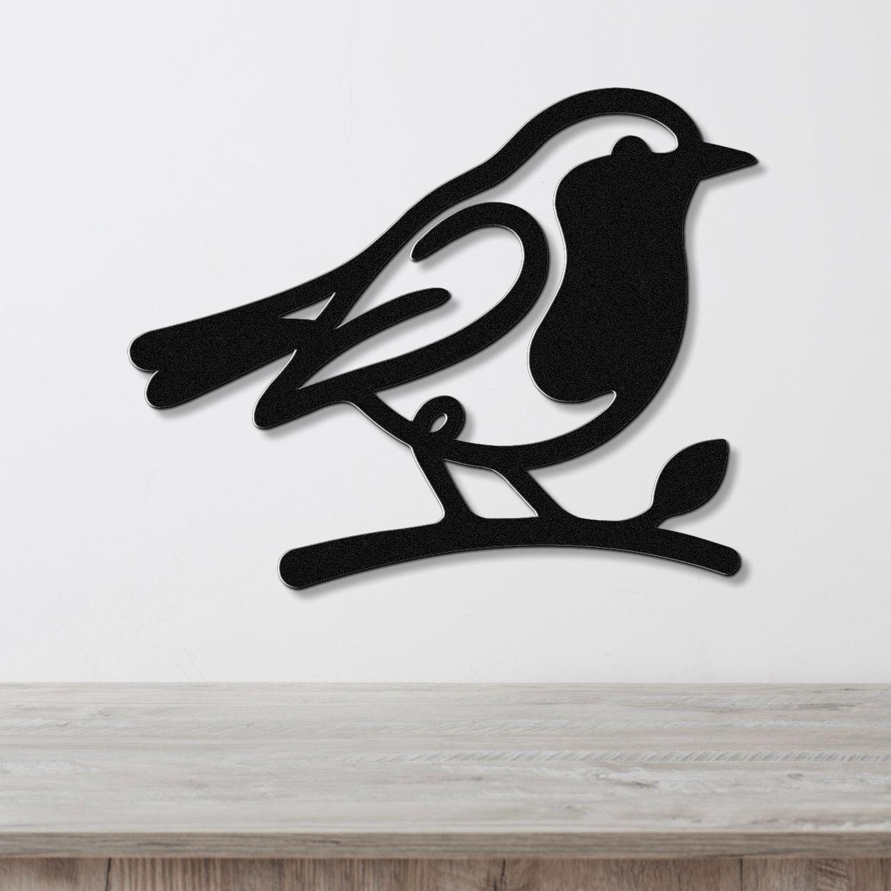 Black metal robin wall art silhouette perched on a branch, mounted on a white wall above a light wood counter.