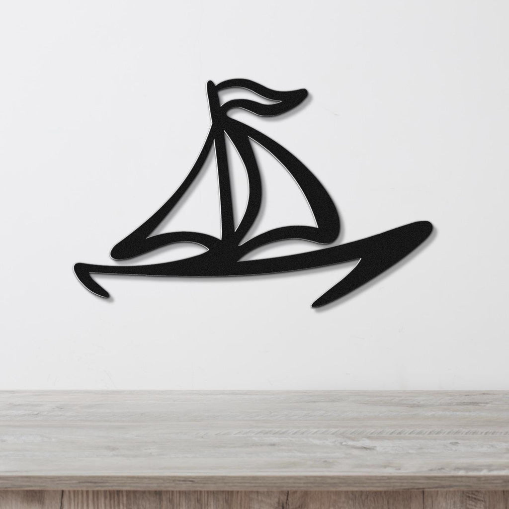 Black metal sailboat wall art with a silhouette design and internal cutout details, mounted on a white wall above a light wood surface.