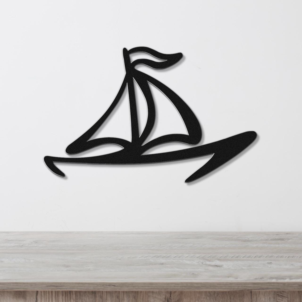 Black metal sailboat wall art with a silhouette design and internal cutout details, mounted on a white wall above a light wood surface.