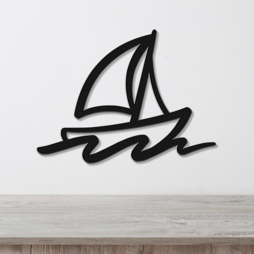 Black metal sailboat wall art with bold lines and wave cutouts, mounted on a white wall above a wooden surface.