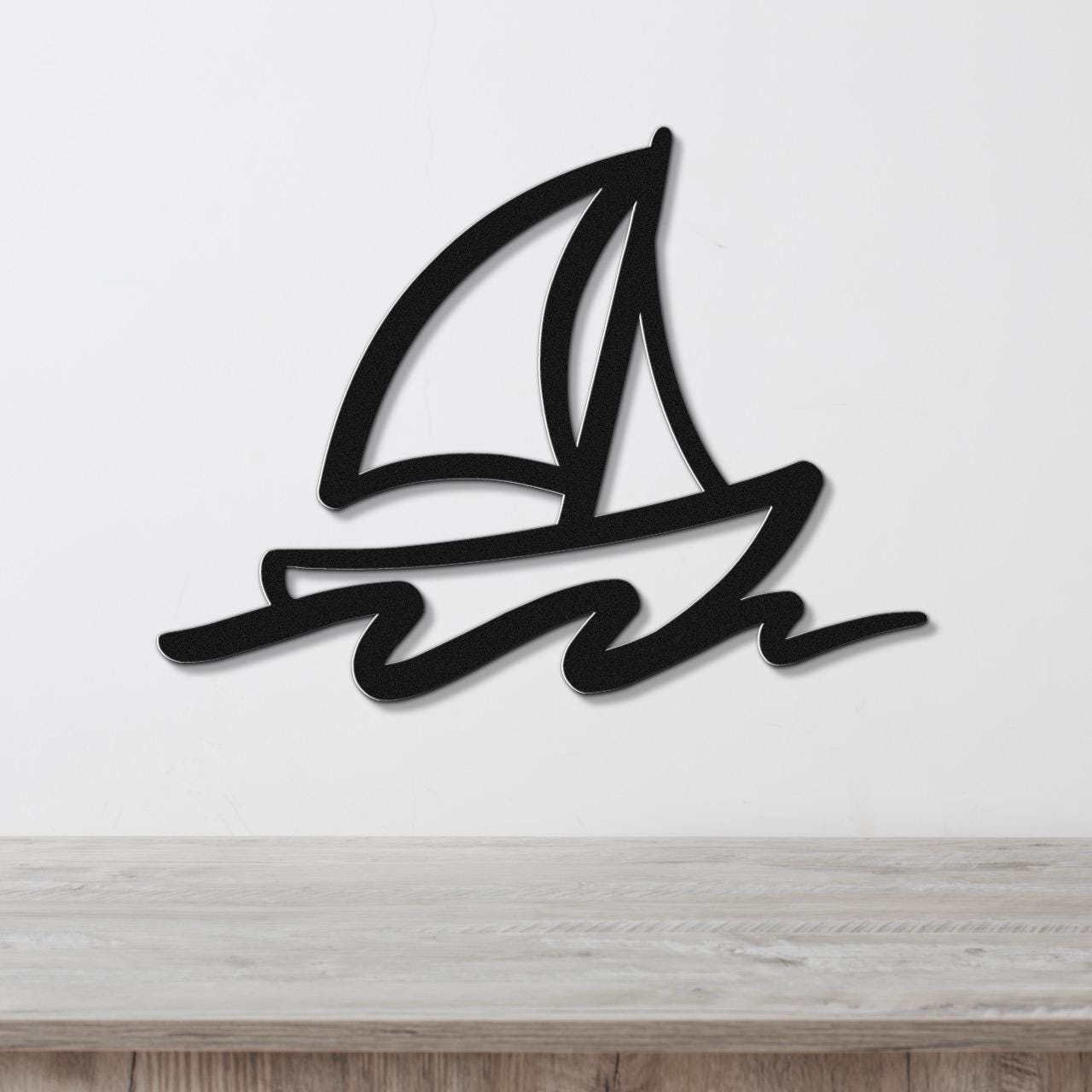 Black metal sailboat wall art with bold lines and wave cutouts, mounted on a white wall above a wooden surface.