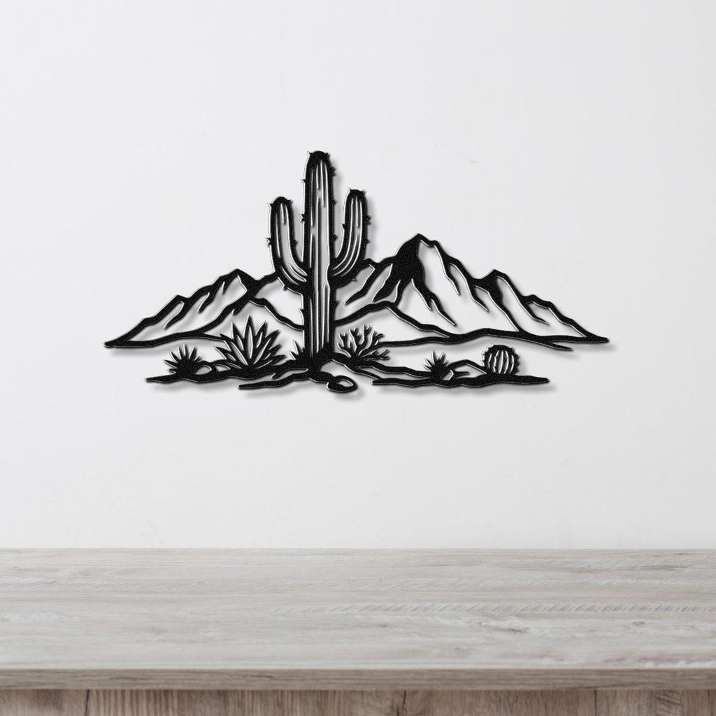 Black metal wall art silhouette of a saguaro cactus and desert landscape with mountains and smaller cacti, mounted on a white wall above a light wood surface.