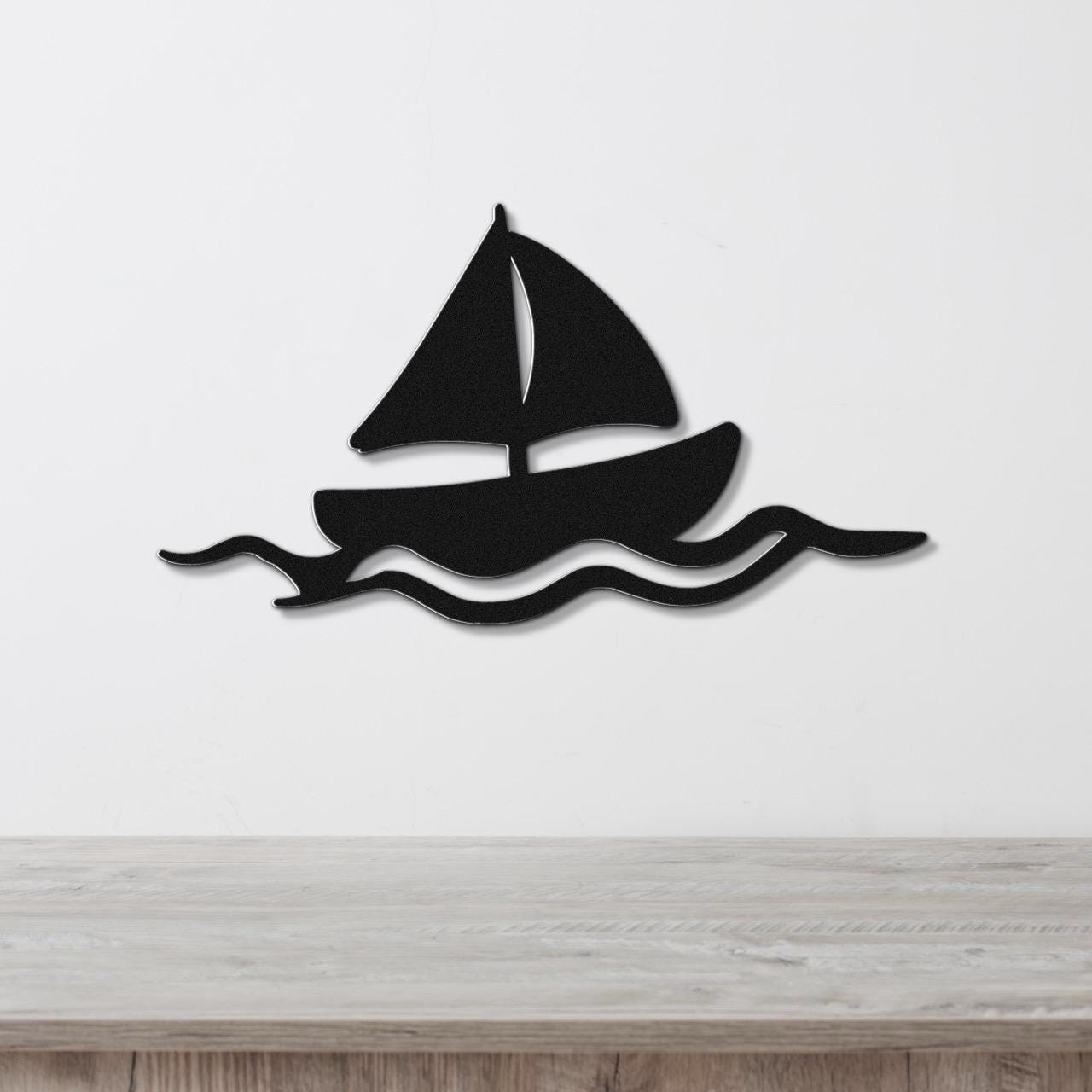 Black metal sailboat wall art with wave cutouts, mounted on a white wall above a wooden surface.